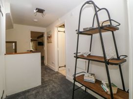 A hallway with a metal and wood shelving unit holding books and decorative items at Meadow Thatch in Cockington