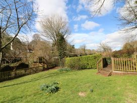 A garden with grass daffodils trees wooden fence and steps leading to a deck at Meadow Thatch in Cockington