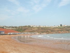 A beach with beach huts along the shore and houses on a hill in the background at Meadow Thatch in Cockington