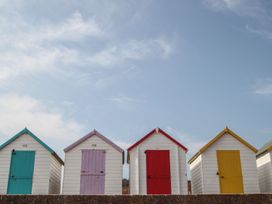 A row of small beach huts with doors painted turquoise purple red and yellow under a blue sky at Meadow Thatch in Cockington