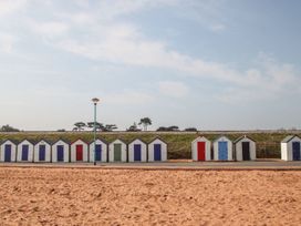 A row of small beach huts with colored doors and a sandy beach in front at Meadow Thatch in Cockington