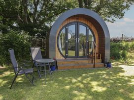 A small pod with a round door and glass panels with stairs outside and two chairs and a table on the grass at Florence Pod in Pembroke