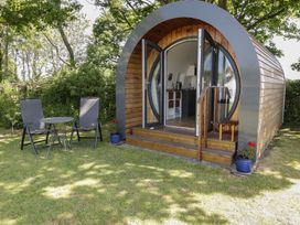 A wooden pod with open double doors leading to a kitchenette outside two chairs and a small table on a lawn with trees in the background at Florence Pod in Pembroke