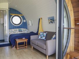 A bedroom with a bed a small wooden table a gray sofa and a round window at Florence Pod in Pembroke