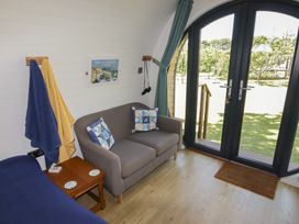A small living area with a gray sofa, two cushions, a wooden side table, blue and yellow towels, and glass doors leading to a garden at Florence Pod in Pembroke