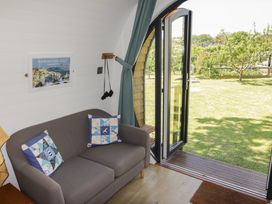 A small living area with a gray sofa and two decorative pillows next to an open glass door showing a grassy garden at Florence Pod in Pembroke