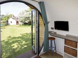 An interior view of a pod with an open round door showing a garden outside a stool a countertop with a mounted tv and wicker baskets at Florence Pod in Pembroke