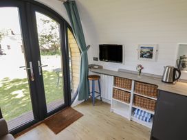 A room with double glass doors leading to a garden with a round table outside a countertop with wicker baskets a kettle a stool a mounted tv and a framed picture at Florence Pod in Pembroke