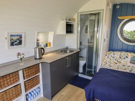 A small room with a kitchenette, sink, microwave, wicker baskets, a bed, and a round window at Florence Pod in Pembroke