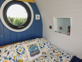 A bedroom with a round window a bed with patterned bedding and a pillow with pembroke text and a small recessed shelf with books at Florence Pod in Pembroke