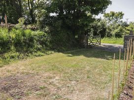A grassy yard with wooden stakes and a metal gate opening to a gravel path surrounded by trees at Florence Pod in Pembroke