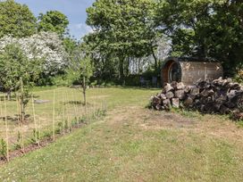 A garden with new plants supported by sticks a woodpile a wooden pod and two chairs at Florence Pod in Pembroke