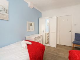 A bedroom with a single bed with red blanket and towels a white wardrobe and dresser a blue chair and a door at Old Malthouse Apartment in Weymouth