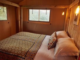 A bedroom with a bed covered with patterned blankets and pillows inside a wooden and fabric room with windows and lights at Braeburn Lodge in Coxbridge near Glastonbury