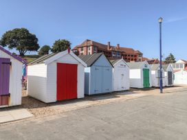 A row of beach huts with trees and a building in the background at 6 The Mews in Felixstowe, Suffolk
