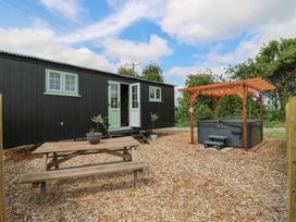 An outdoor area with a wooden picnic table potted plants a black building with green windows and doors and a hot tub under a wooden pergola at The Heron in Lode near Bottisham