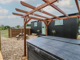 An outdoor area with a covered hot tub, a wooden pergola with hanging lights, a black cabin with a mint green door and windows, and a wooden picnic table surrounded by wood chips