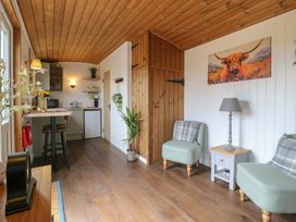 A small living area with two chairs a side table and lamp next to a kitchenette with stools and wooden ceiling at The Heron in Lode near Bottisham