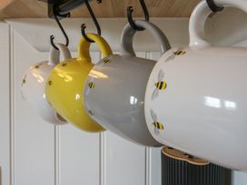 Four ceramic mugs with bee patterns hanging on hooks in a kitchen at The Heron in Lode near Bottisham