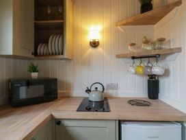 A kitchen corner with a microwave oven a kettle on a stovetop hanging mugs and dishes on shelves at The Heron in Lode near Bottisham