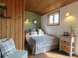 A bedroom with a double bed gray and white bedding a small window and a bedside table with a clock and flowers at The Heron in Lode near Bottisham