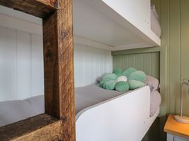 A bunk bed with a flower-shaped pillow on the lower bunk next to a wooden ladder and a bedside table with a lamp at The Heron in Lode near Bottisham