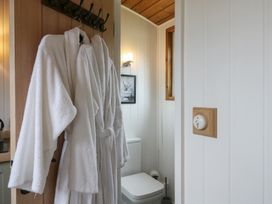 Two white bathrobes hanging on hooks on a wooden door next to a bathroom with a toilet and a framed picture at The Heron in Lode near Bottisham