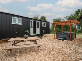 An outdoor area with a wooden picnic table a black caravan with mint green windows and doors and a hot tub with wooden pergola at The Heron in Lode near Bottisham