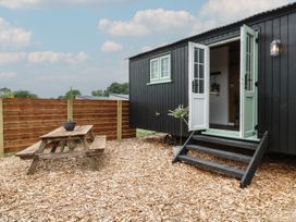 An outdoor area with a wooden picnic table and a small building with open double doors at The Heron in Lode near Bottisham