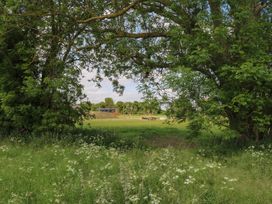 A grassy field with white flowers framed by trees with a picnic table and building in the distance at The Heron in Lode near Bottisham