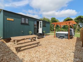 An outdoor area with a green wooden cabin labeled Barn Owl a wooden picnic table and a hot tub under a wooden pergola at Barn Owl in Lode near Bottisham