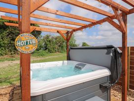 An outdoor hot tub under a wooden pergola with string lights and a sign that says Welcome to the hot tub sit back and relax at Barn Owl in Lode near Bottisham