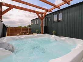 An outdoor hot tub with bubbling water under a wooden pergola next to a dark green cabin with two windows and a door at Barn Owl in Lode near Bottisham