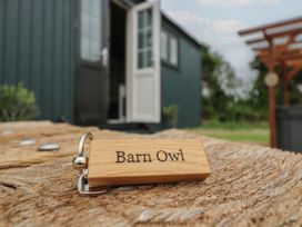 A wooden keychain with Barn Owl text on a wooden surface outside a dark green building with an open door at Barn Owl in Lode near Bottisham