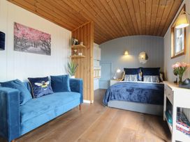 A bedroom with a blue sofa a bed white furniture and wooden ceiling at Barn Owl in Lode near Bottisham