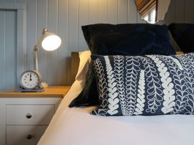 A bedside table with a lamp and clock next to a bed with patterned and plain pillows at Barn Owl in Lode near Bottisham