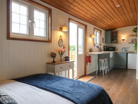 A small room with a bed a side table with flowers and a vintage phone an open door leading outside and a kitchenette with a countertop and stools at Barn Owl in Lode near Bottisham