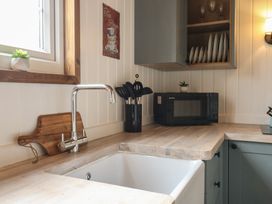 A kitchen corner with a sink a faucet a wooden cutting board kitchen utensils a microwave and a cabinet with plates at Barn Owl in Lode near Bottisham