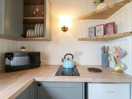 A kitchen counter with a microwave kettle cups and shelves with tins at Barn Owl in Lode near Bottisham