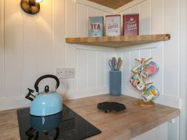 A kitchen corner with a blue kettle on the stove mugs on a wooden stand and tins on a wooden shelf at Barn Owl in Lode near Bottisham