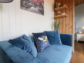A blue sofa with three cushions including one with a bee design in a room with white and wood paneled walls and shelves with small items at Barn Owl in Lode near Bottisham