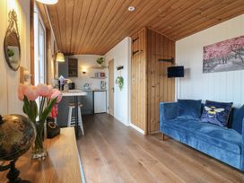 A living area with a blue sofa a small kitchen with a counter stools and wooden ceiling at Barn Owl in Lode near Bottisham