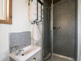 A bathroom with a sink a mirror a towel rack with rolled towels and a shower area at Barn Owl in Lode near Bottisham