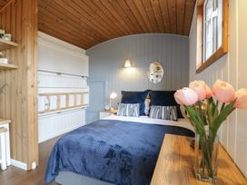 A bedroom with a bed with blue covers and pillows a wooden ceiling and a vase with pink flowers on a wooden table at Barn Owl in Lode near Bottisham