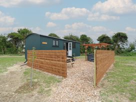 An outdoor area with a small green building labeled Barn Owl surrounded by wooden fences and a pergola over a black hot tub at Barn Owl in Lode near Bottisham