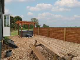 An outdoor area with a wooden picnic table a covered hot tub a wooden fence and an open door at Barn Owl in Lode near Bottisham