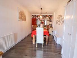 A dining room with a wooden dining table covered with a red tablecloth and wooden chairs in front of a floral wallpapered wall at 67 Pendre Avenue in Prestatyn