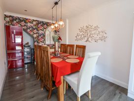 A dining room with a wooden table covered with a red tablecloth and six wooden chairs and one white chair a floral wallpaper wall with a red refrigerator and decorative lighting at 67 Pendre Avenue in Prestatyn
