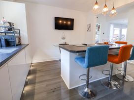 A kitchen with a counter and colorful bar stools a wall-mounted television and pendant lights at 67 Pendre Avenue in Prestatyn