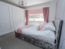 A bedroom with a bed with pillows and blankets a window with curtains a chandelier and built in white wardrobes at 67 Pendre Avenue in Prestatyn